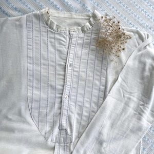 May include: A white long-sleeved shirt with a striped collar and a button-up front. The shirt has a relaxed fit and is made of a soft, comfortable fabric.