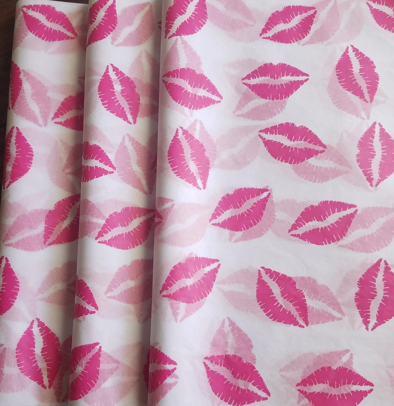 May include: White wrapping paper with a repeating pattern of bright pink lips. The lips are stylized and evenly spaced across the paper, creating a playful and feminine design. The paper is folded, showing the texture and layers.