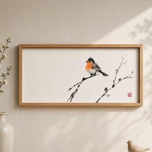 Könnte beinhalten: Ein rechteckiges gerahmtes Wandbild mit einer Tuschezeichnung eines kleinen Vogels mit orangefarbener Brust, der auf einem dünnen, dunklen Ast sitzt. Das Kunstwerk ist auf weißem Hintergrund und enthält einen kleinen roten quadratischen Stempel.