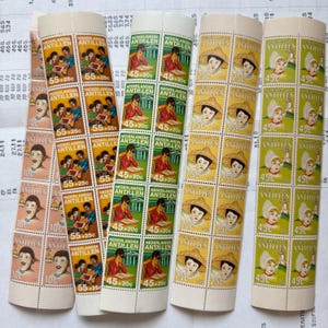 Può includere: Diversi rotoli di francobolli vintage delle Antille Olandesi. I francobolli presentano vari disegni, tra cui ritratti, bambini che leggono e donne con copricapi tradizionali. I valori sono 10¢, 25¢, 45¢ e 55¢.