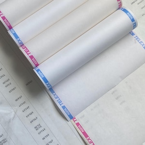 May include: Several rolls of white paper are visible, with blue and pink striped tape reading "ASPA TELEX" along the edges. The rolls are partially unrolled, revealing the paper's texture. The background includes a sheet with printed numbers.