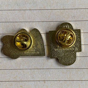 May include: Two gold-colored metal pins. The first pin is shaped like the McDonald's golden arches logo. The back of the pin says "McDonald's 1998-2000 TM". The second pin is shaped like a square with rounded corners. The back of the pin says "&copy;2000 McDonald's TM".