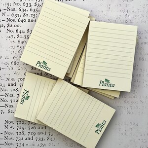 May include: A stack of yellow lined notepad paper with a green logo that says "Planta" on each sheet. The paper is stacked on a table with a white surface.