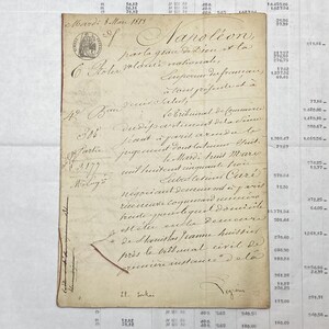 May include: A vintage, rectangular, off-white document featuring handwritten French cursive script in dark ink. The paper displays a circular imperial seal in the top left corner and includes the text Napoléon, par la grâce de Dieu et la volonté nationale.