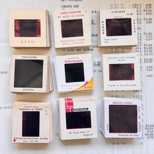 Può includere: Una collezione di diapositive vintage da 35 mm, presentate in cornici di cartone bianco. Le diapositive presentano vari soggetti e includono testo in francese e inglese. Luoghi come Firenze e Parigi sono annotati.