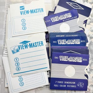 Könnte beinhalten: Eine Sammlung von Vintage View-Master-Rollen und -Hüllen. Die Hüllen sind weiß und blau, mit den Wörtern "VIEW-MASTER" und "GAF" aufgedruckt. Die Rollen befinden sich in blauen und weißen Hüllen mit dem Text "7 THREE DIMENSION FULL COLOR PICTURES".