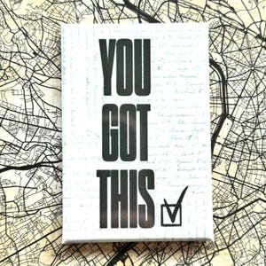 Op de afbeelding: Een rechthoekige canvas print met de tekst "YOU GOT THIS" in vette zwarte letters. Een vinkje staat in een zwart vierkantje onderaan. De achtergrond heeft een vintage kaartontwerp met handschrift.