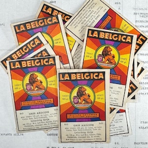 Könnte beinhalten: Eine Sammlung von Vintage-Papierkarten mit dem Text "LA BELGICA". Jede Karte zeigt ein Löwenemblem in einem kreisförmigen Design, mit Text in mehreren Sprachen und einem lebendigen Farbschema aus Rot, Orange und Gelb.