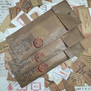 May include: A collection of vintage brown paper envelopes with red stamps and various paper scraps. The envelopes are stacked on top of each other and have a worn, aged look. The paper scraps include old postage stamps, labels, and other ephemera.