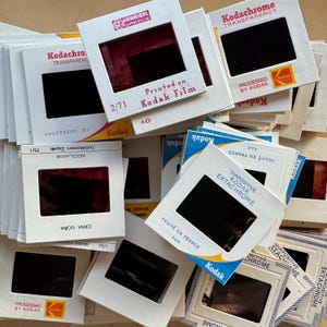 Könnte beinhalten: Ein Stapel von Vintage-Kodak-Diafilm-Dosen, einige mit dem Text "Kodachrome Transparency" und "Processed by Kodak". Die Dosen sind in verschiedenen Farben, darunter Rot, Blau und Gelb.