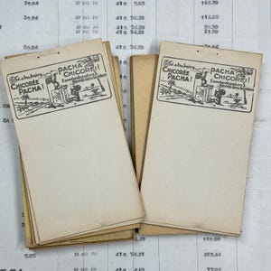 Op de afbeelding: Een stapel vintage papieren reclamekaartjes voor Pacha Chicoree, een koffiesurrogaat. De kaartjes tonen een zwart-witte illustratie van een man die een kop koffie vasthoudt en een aap die op een vat zit. De tekst op de kaartjes luidt "Ein a buboire Chicoree Pacha! EensGedronken. Steeds Geschonken."