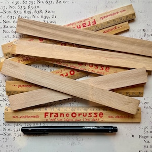 Puede incluir: Un primer plano de reglas de madera con texto rojo y negro. Las reglas est&aacute;n apiladas unas sobre otras y tienen diferentes medidas. El texto en las reglas dice "Franc Orusse" y "un entremets c'est un r&eacute;gal que l'on sert... au dessert..."