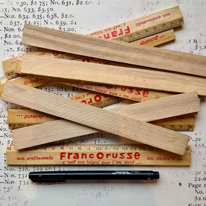 Puede incluir: Un primer plano de reglas de madera con texto rojo y negro. Las reglas est&aacute;n apiladas unas sobre otras y tienen diferentes medidas. El texto en las reglas dice "Franc Orusse" y "un entremets c'est un r&eacute;gal que l'on sert... au dessert..."