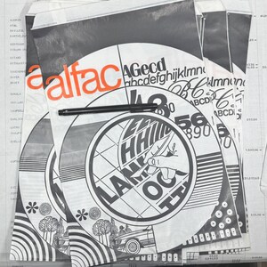 Op de afbeelding: Een stapel vintage grafisch ontwerp materialen. De ontwerpen bevatten het woord "alfac" in oranje, samen met verschillende lettertypen, cijfers en illustraties. Een zwarte pen ligt bovenop de papieren, met een lijst met namen op de achtergrond.