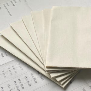May include: A stack of off-white, rectangular paper sheets fanned out, with a few sheets stacked on top. The paper is on top of a printed document with text and numbers. The paper has a slightly textured surface.