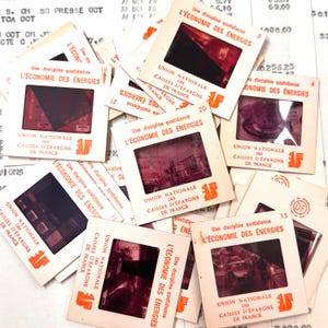 May include: A pile of vintage French slides. Each slide has the text "L'ÉCONOMIE DES ÉNERGIES" and "UNION NATIONALE DES CAISSES D'ÉPARGNE DE FRANCE". The slides have orange and white text and images, with a retro aesthetic.