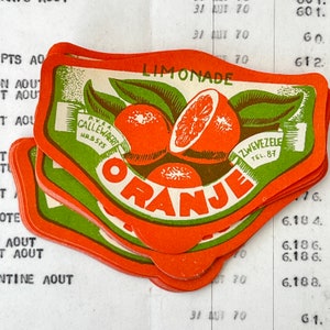 Op de afbeelding: Stapel oranje en groene papieren etiketten met de tekst "Limonade Oranje" en "P.V.&A. Callewaert HR.B.575" en "Zwevezele Tel. 87".