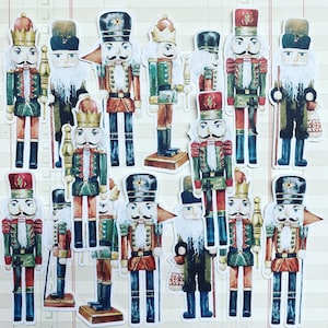 Könnte beinhalten: Eine Sammlung von 13 bunten Nussknackerfiguren mit verschiedenen Designs. Die Nussknacker sind aus Holz und in leuchtenden Farben bemalt, darunter Rot, Blau, Grün und Gold. Sie tragen alle traditionelle Nussknackerkostüme und haben unterschiedliche Gesichtsausdrücke.
