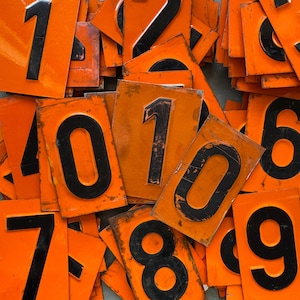 Könnte beinhalten: Eine Sammlung von orangefarbenen und schwarzen nummerierten Kacheln. Die Zahlen 1, 2, 3, 4, 5, 6, 7, 8, 9 und 0 sind sichtbar.