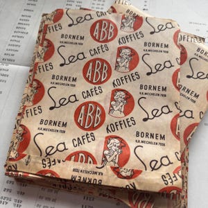 May include: A stack of vintage paper coffee bags. The bags are beige with a repeating pattern of red circles with the letters "ABB", the words "Sea Caf&eacute;s" and "Koffies", and an illustration of a woman drinking coffee. The text "Bornem H.R. Mechelen 7036" is also printed on the bags.