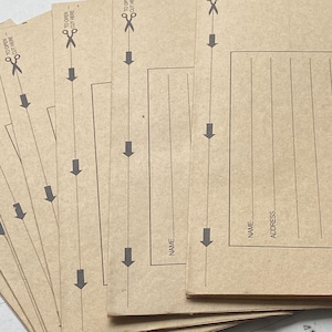 Könnte beinhalten: Ein Stapel brauner Kraftpapierumschläge. Jeder Umschlag hat eine gepunktete Linie mit einem Pfeil, den Text "TO OPEN - CUT HERE" und Platz für Name und Adresse. Der Text ist dunkelgrau.