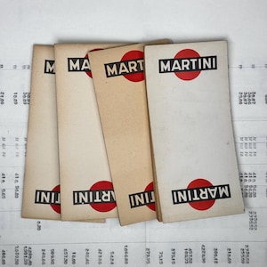 Può includere: Un mazzo di sei carte di carta vintage con la parola "MARTINI" stampata in lettere nere con un cerchio rosso attorno alla parola. Le carte sono tutte di dimensioni leggermente diverse e sono impilate l'una sull'altra.