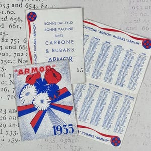 Può includere: Tre articoli di carta vintage con l'anno 1935, tra cui un calendario con i mesi in francese e il testo "BONNE DACTYLO BONNE MACHINE MAIS CARBONE & RUBANS ARMOR". Le grafiche presentano motivi floreali e nastri di colore rosso, bianco e blu.