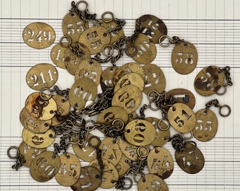 May include: A collection of brass tags with numbers on them, connected by a chain. The tags are arranged in a random pattern and some of the numbers are visible, including 24, 21, 60, 58, and 55.