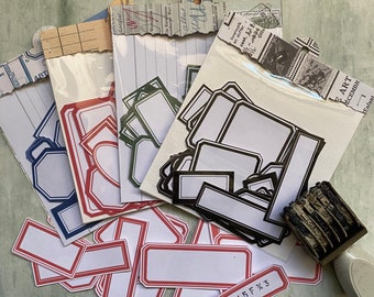 May include: Assortment of blank labels in various sizes and colors, including red, blue, and black. The labels are arranged on a textured surface. Some labels have a decorative border. The text "8/5F*3" is visible on one of the labels.