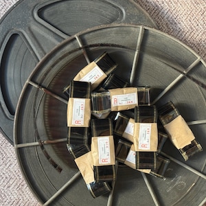 May include: A close-up of several rolls of film labeled with the letters "R" and "OSS" and numbers. The film is sitting inside a metal film reel.