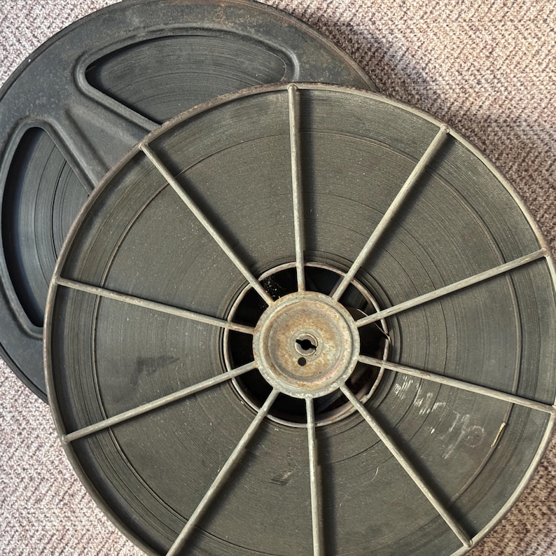 May include: Two vintage film reels with metal spools and black film. The reels are stacked on top of each other.