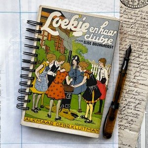Pode incluir: Um livro infantil vintage intitulado "Loekie en haar Jubje" de Elise Bronkhorst. A capa apresenta uma ilustração colorida de cinco meninas com vestidos, com uma menina de cabelo ruivo no centro segurando uma panela. O livro é encadernado em espiral e tem um fundo branco.