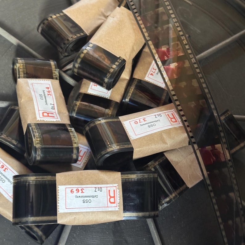 May include: A close-up of several rolls of 35mm film, wrapped in brown paper with labels that include the text "OSS", "Z30", and "369".