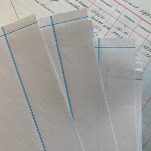 K&ouml;nnte beinhalten: Ein Stapel wei&szlig;es, liniertes Papier mit blauen Linien. Das Papier ist in der Mitte gefaltet und die Kanten sind sichtbar. Das Papier ist leer und es ist nichts darauf geschrieben.