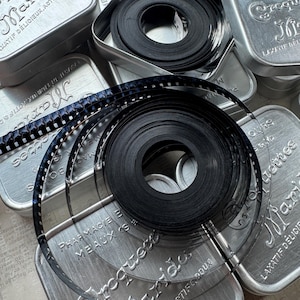 May include: Close-up of a collection of vintage film reels in metal tins. The reels are labeled with the words "Marot" and "Laxatif Delicieux".