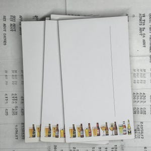 May include: Three white cards with a row of colorful beer bottles printed at the bottom. The cards are blank and have a line for writing.