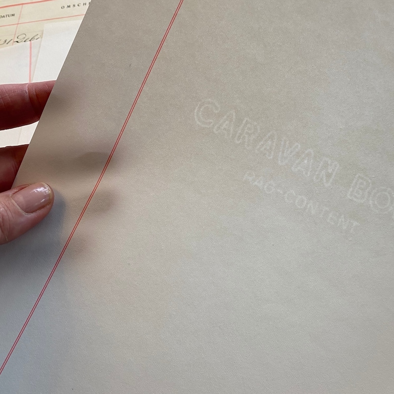 May include: A white sheet of paper with a red line drawn diagonally across it. The words "CARAVAN BOX" are embossed in white on the paper, with the words "RAG-CONTENT" underneath.