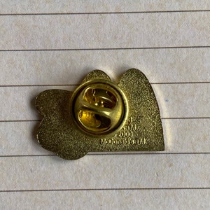 May include: Gold-colored metal pin featuring two hearts with the text "McDonald's TM 2000" on the back.