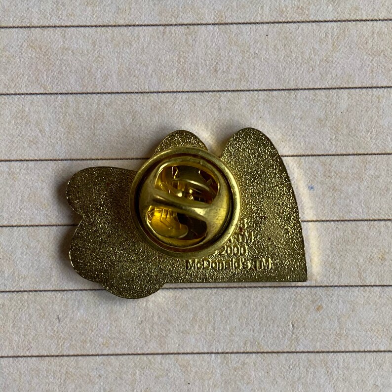 May include: Gold-colored metal pin featuring two hearts with the text "McDonald's TM 2000" on the back.