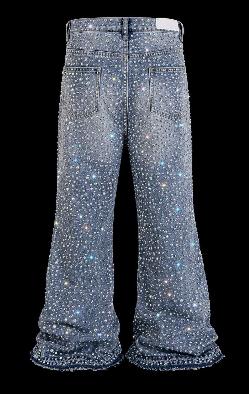 May include: Light blue denim jeans heavily embellished with sparkling rhinestones. The jeans have a flared leg design and feature classic five-pocket styling. The rhinestones are densely applied, creating a shimmering effect across the entire garment.