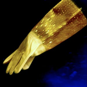 May include: A pair of elegant, light yellow gloves. The gloves have a long, shimmering gold sequined upper section. The gloves are set against a dark blue and black background, creating a striking contrast.
