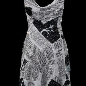 May include: A sleeveless dress featuring a cowl neckline and thin, sparkling chain straps. The fabric is covered in a black and white newspaper print pattern with scattered, shimmering rhinestone embellishments throughout the entire garment.
