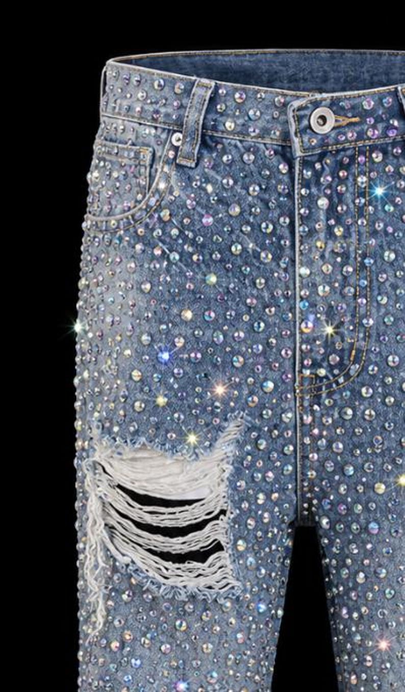 May include: Light blue denim jeans heavily embellished with iridescent rhinestones. The jeans feature a distressed, ripped knee detail. The overall effect is a sparkling, glamorous look.