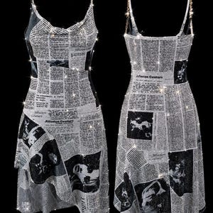 May include: A sleeveless dress featuring a newspaper print pattern with black text and images on a silver, sparkling background. The garment has a cowl neckline, thin chain straps, and an asymmetrical hemline with the text Jillusion Couture.