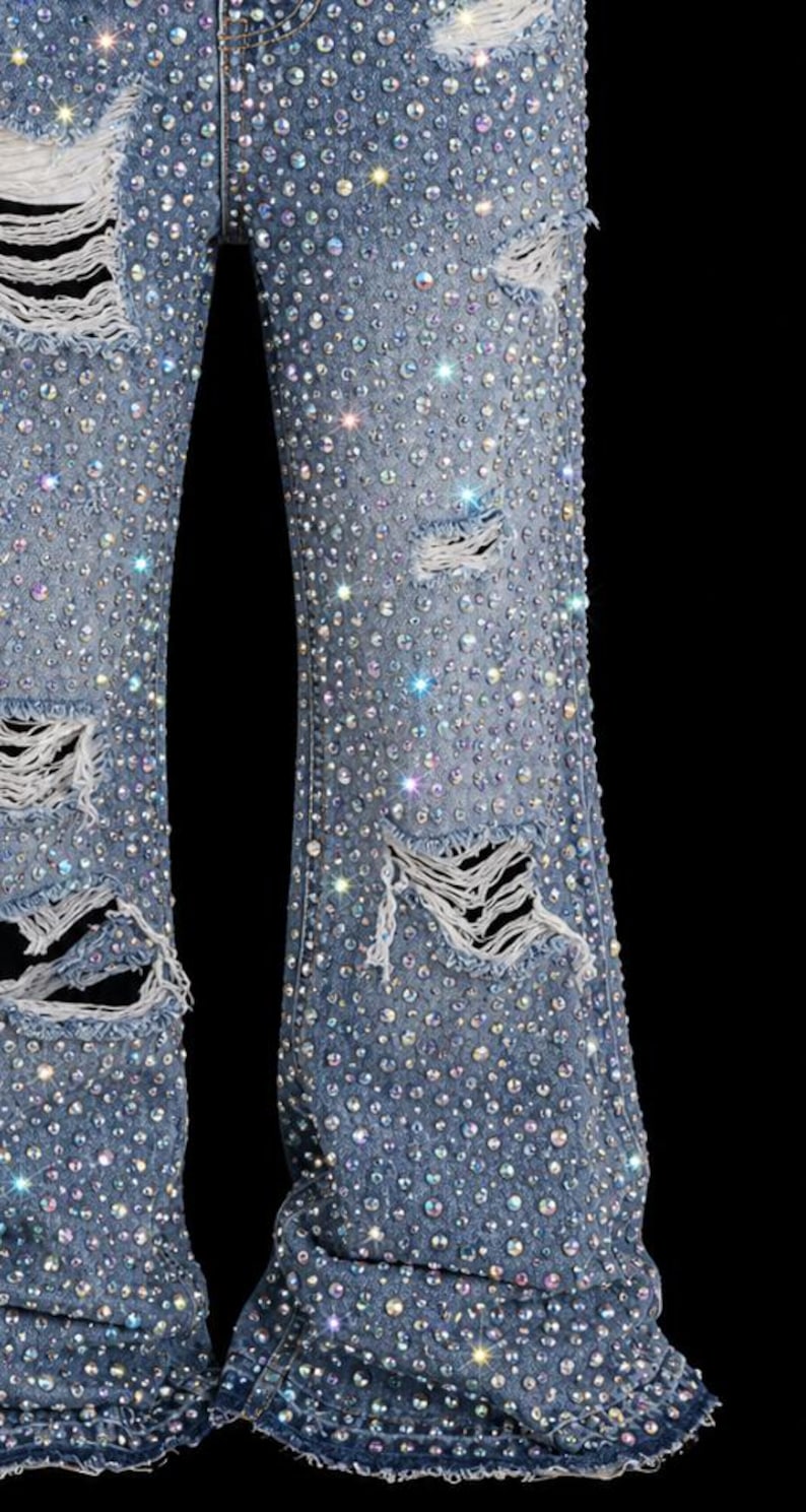 May include: Light blue denim jeans heavily embellished with sparkling rhinestones. The jeans feature distressed details with ripped sections, creating a glamorous and edgy aesthetic. The rhinestones are of varying sizes.