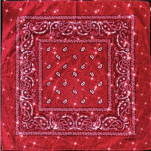May include: Red bandana with a paisley pattern and a sparkling effect. The square cloth features a white border with intricate designs and small white paisley shapes in the center. The text "100% COTTON" is visible at the bottom.