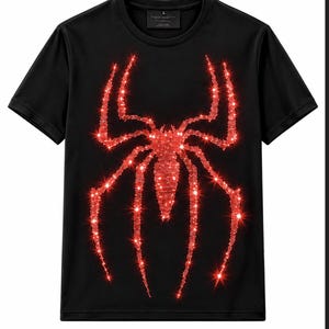 Puede incluir: Una camiseta negra de manga corta con un gráfico de araña grande y centrado compuesto por brillantes pedrería roja. El diseño crea un efecto luminoso y reflectante sobre la tela oscura, con cuello redondo y una etiqueta de talla L en el cuello.