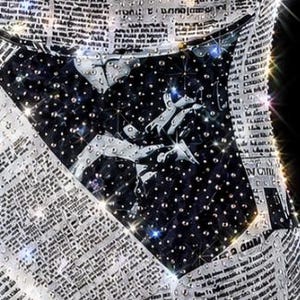 May include: A garment featuring a black and white newspaper print pattern overlaid with numerous clear, reflective crystals. The centre section displays a dark, starry night sky graphic with white constellations and scattered crystal embellishments.