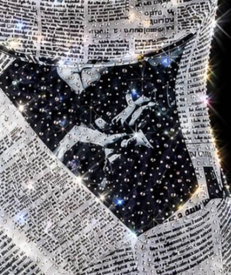 May include: A garment featuring a black and white newspaper print pattern overlaid with numerous clear, reflective crystals. The centre section displays a dark, starry night sky graphic with white constellations and scattered crystal embellishments.