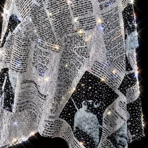 May include: A black and white fabric garment featuring a repeating newspaper print pattern with columns of text and illustrations. The entire surface is densely covered in small, reflective clear crystals that create a sparkling effect.